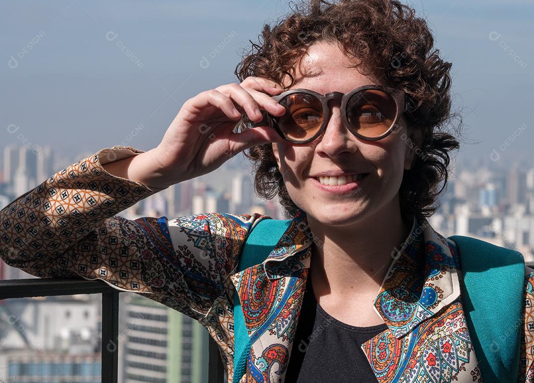 Beautiful, modern woman posing for the camera wearing sunglasses with the city of São Paulo in the background.