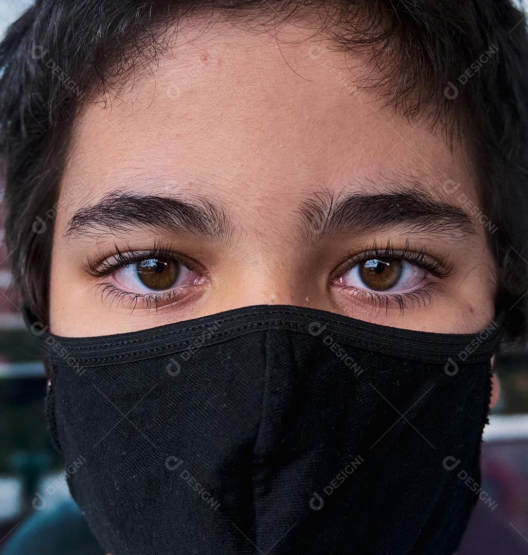Menino brasileiro usando máscara durante a quarentena olhando para fora.