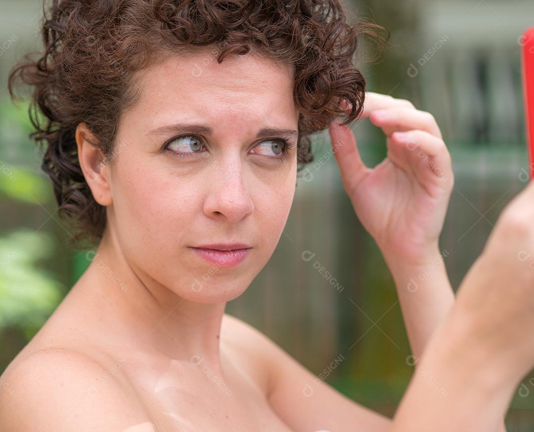 Linda mulher brasileira arrumando o cabelo com espelho na mão.