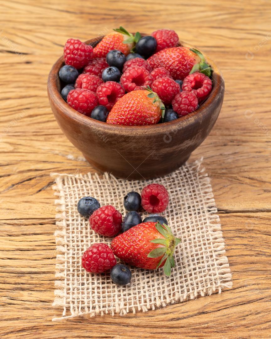 Morangos, mirtilos e framboesas em uma tigela sobre madeira
