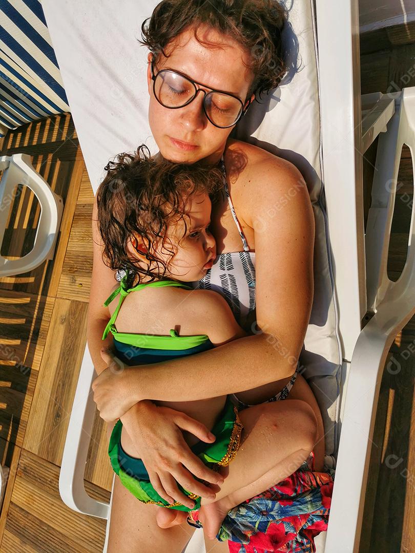 Mãe e filha brasileiras relaxando na cadeira da piscina..