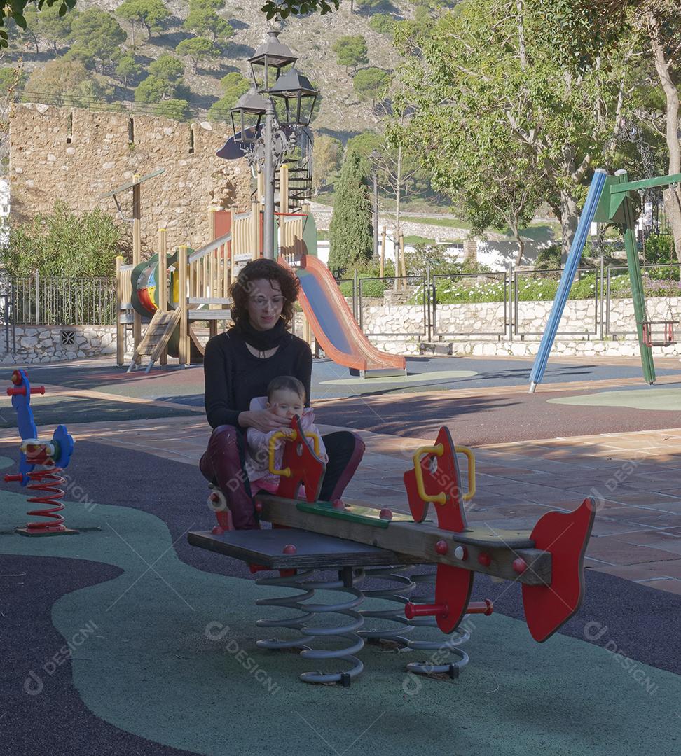 Mãe e filha brincando na gangorra do parque.
