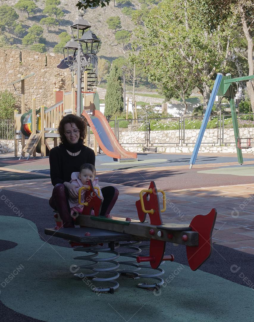 Mãe e filha brincando na gangorra do parque.