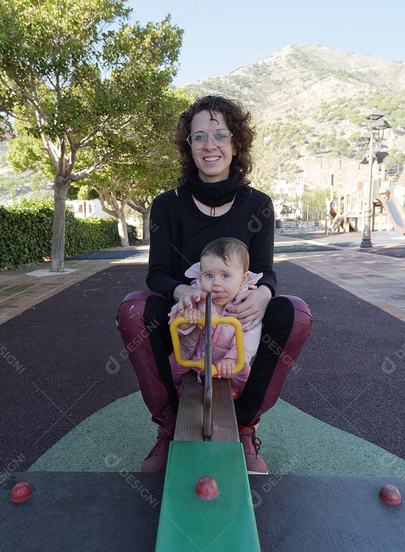 Mãe e filha brincando na gangorra do parque.
