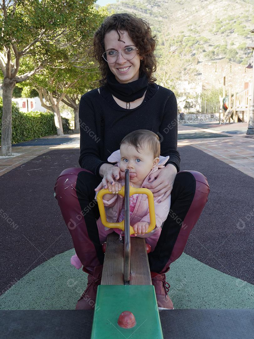 Mãe e filha brincando na gangorra do parque.