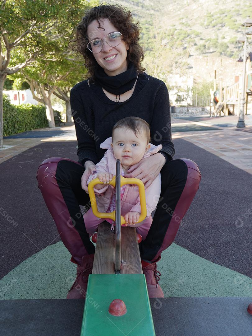 Mãe e filha brincando na gangorra do parque.
