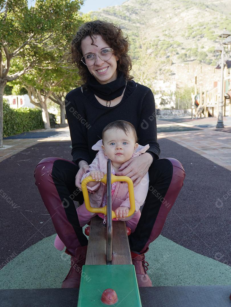 Mãe e filha brincando na gangorra do parque.
