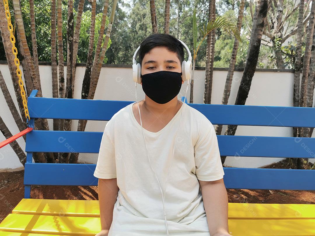 Menino brasileiro entediado usando máscara e fones de ouvido posando para a câmera.