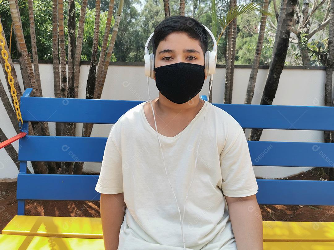Menino brasileiro entediado usando máscara e fones de ouvido posando para a câmera.