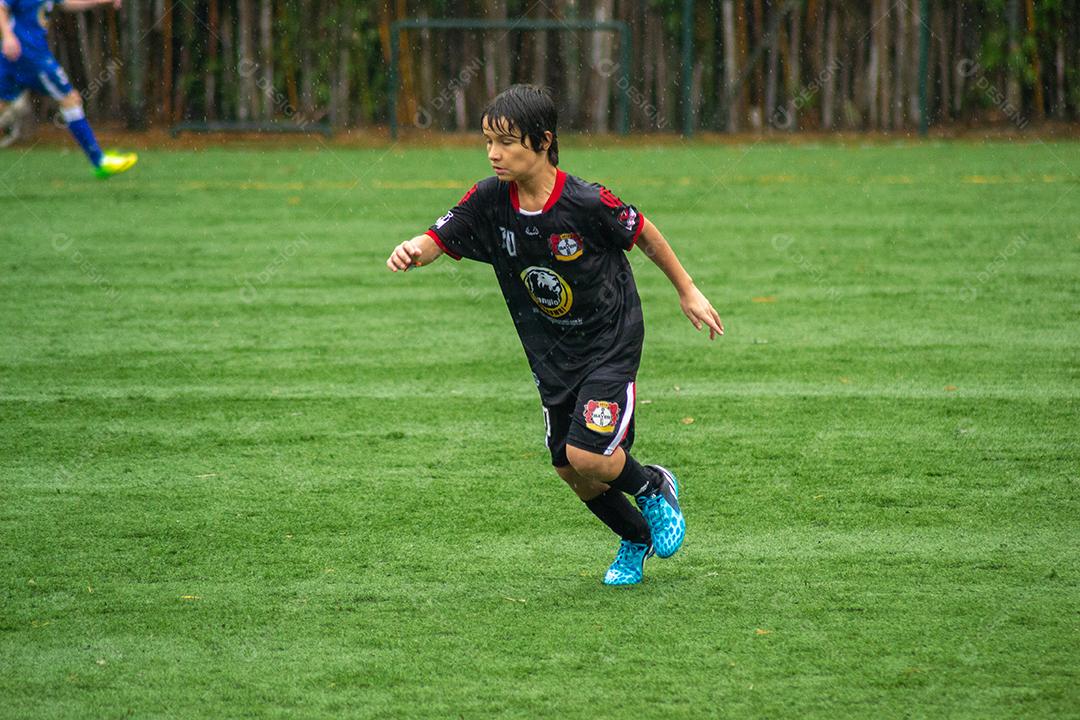 Young Boy correndo no campo de futebol durante a chuva