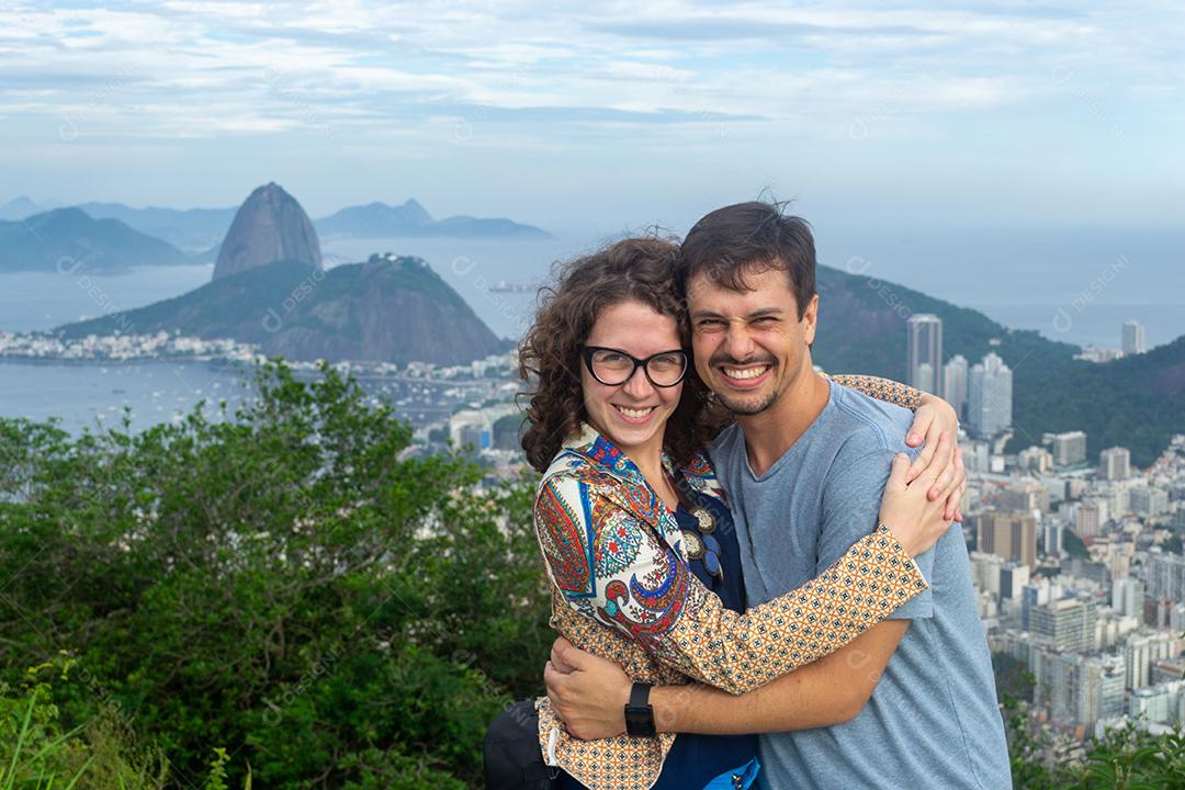 Vista de um casal apaixonado se abraçando com a Baía de Guanabara ao fundo.