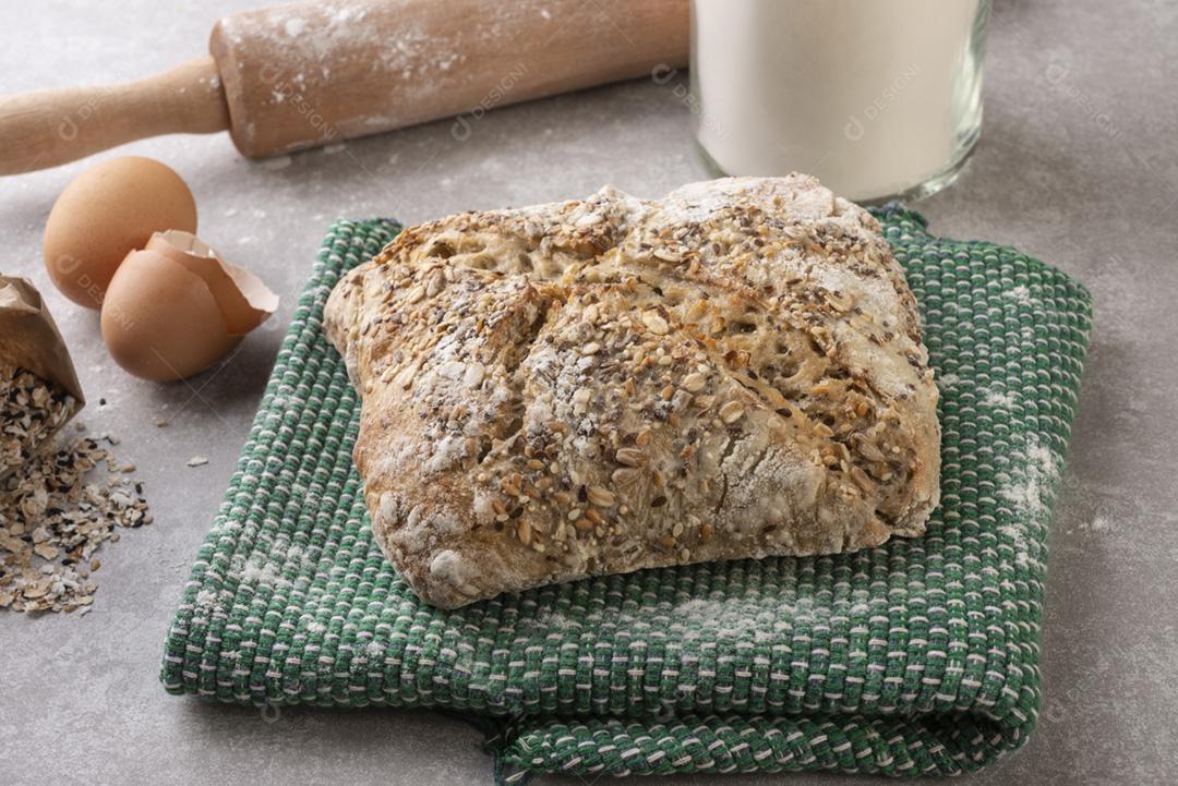 Pão inteiro sobre pano com farinha, ovos e rolo sobre con