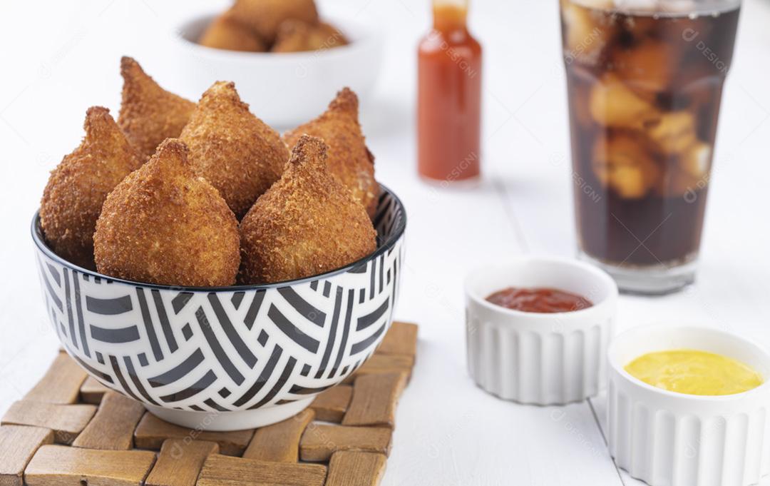 Coxinha de lanche típico brasileiro em uma tigela com copo de refrigerante