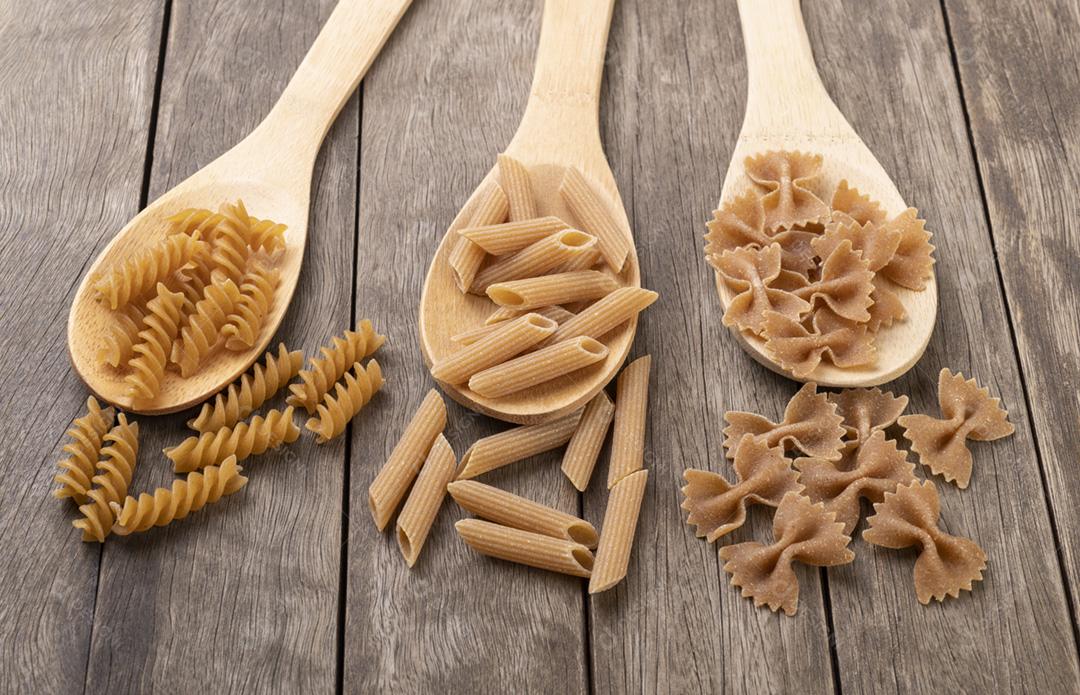 Macarrão de trigo integral sortido em colheres sobre mesa de madeira