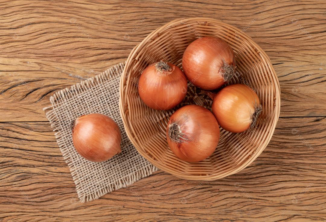 Cebolas em uma cesta sobre a mesa de madeira