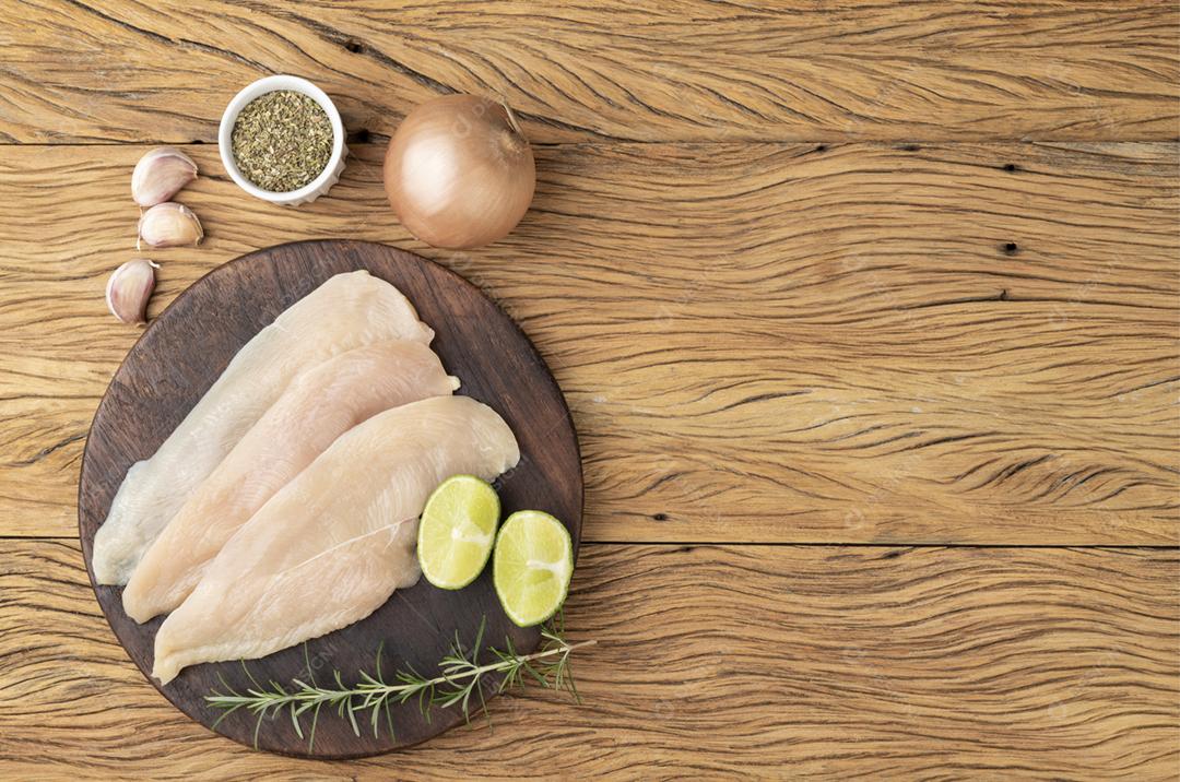 Peito de frango sobre tábua de madeira com temperos e espaço para texto