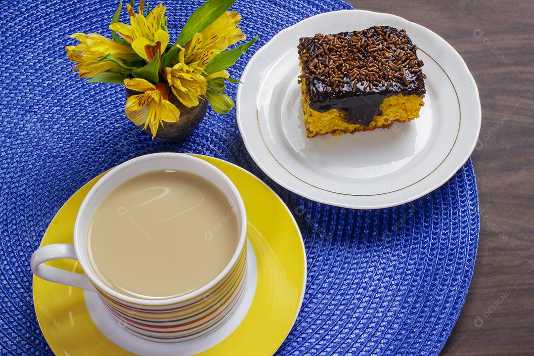 Bolo de cenoura com cobertura de chocolate e xícara de leite com café