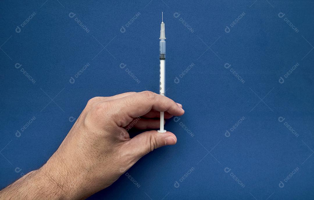 Mão do médico segurando a seringa para vacinar com fundo azul