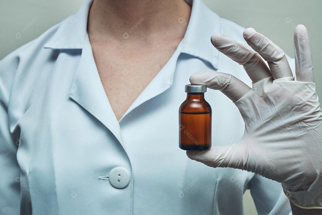 Vista das mãos da enfermeira usando luvas mostrando a ampola de medicamento.