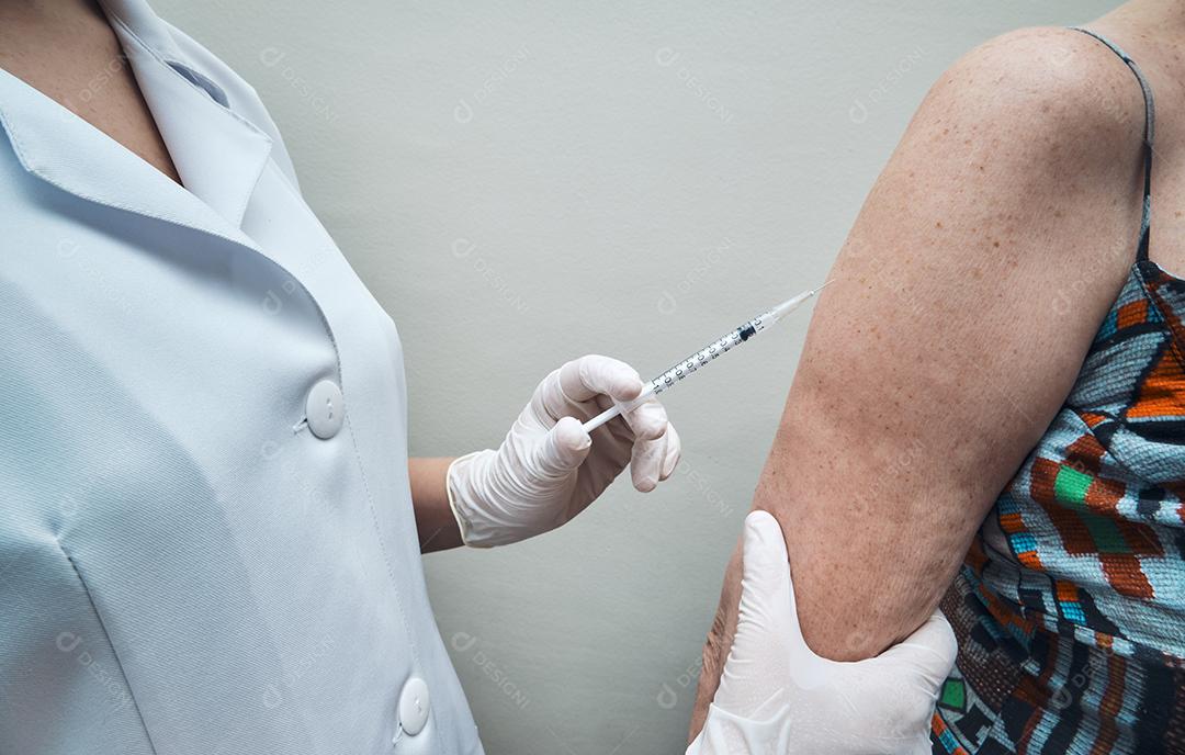 Vista da enfermeira vacinando o braço da mulher idosa.