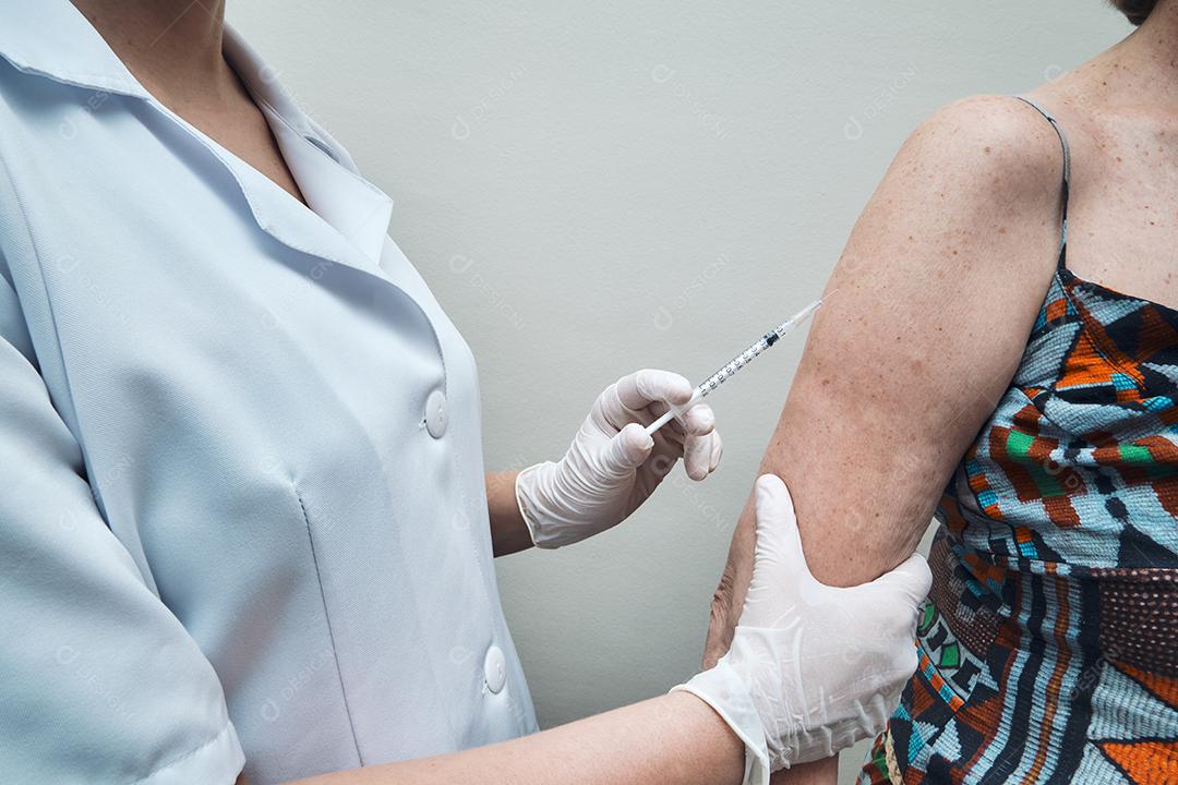 Vista da enfermeira vacinando o braço da mulher idosa.