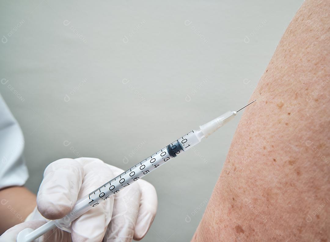 Vista da enfermeira vacinando o braço da mulher idosa.