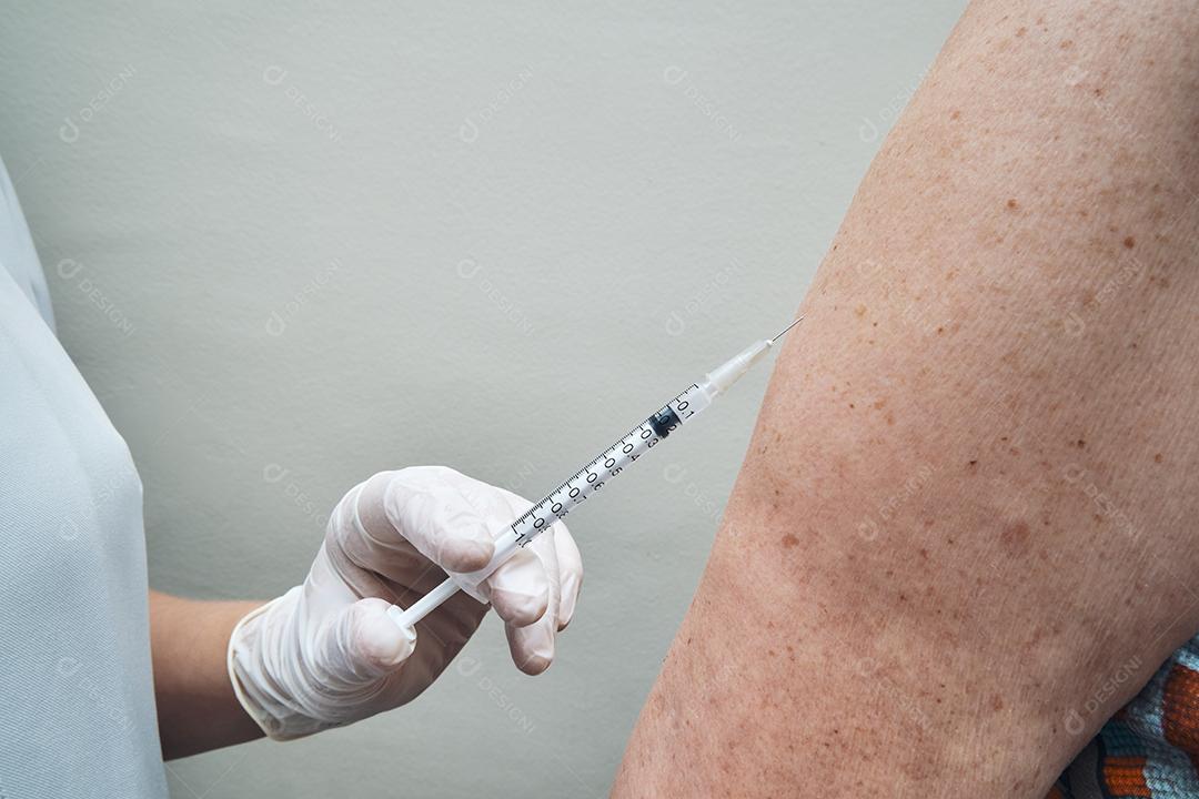 Vista da enfermeira vacinando o braço da mulher idosa.