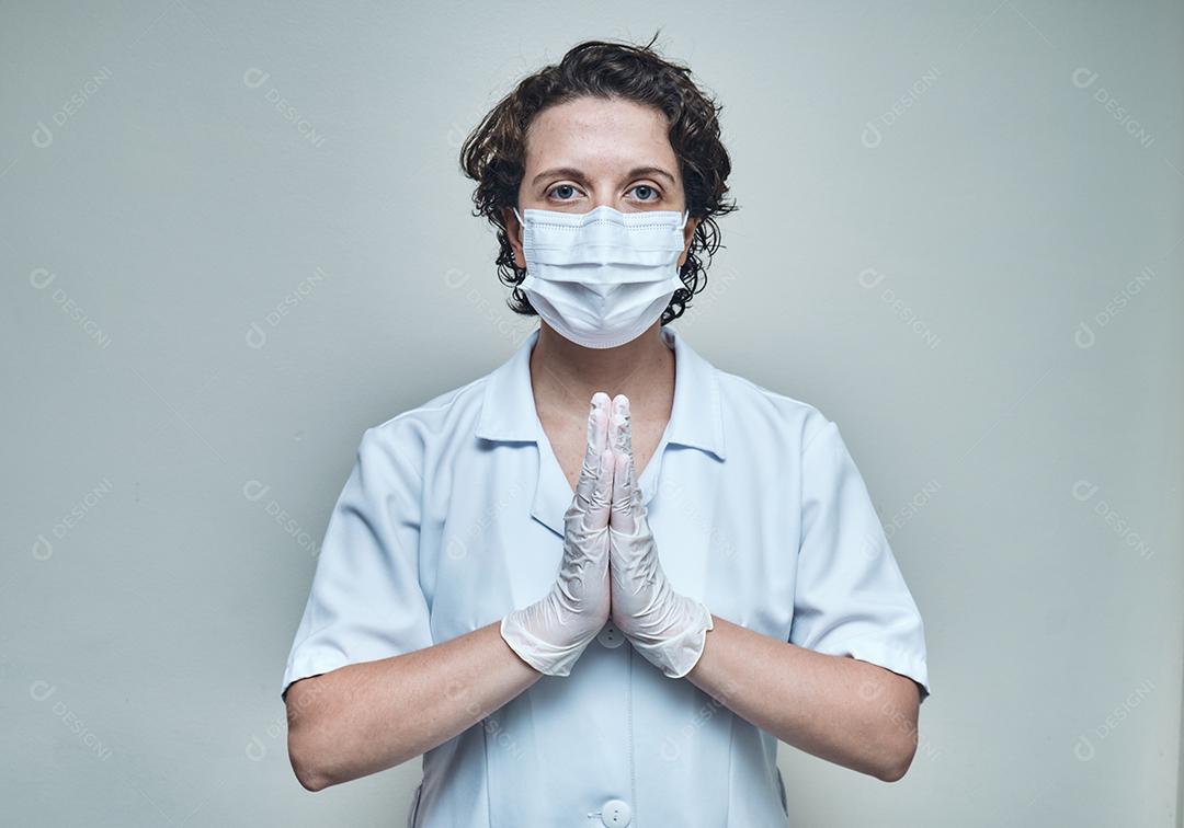 enfermeira usando máscara e luvas orando com as palmas das mãos fechadas