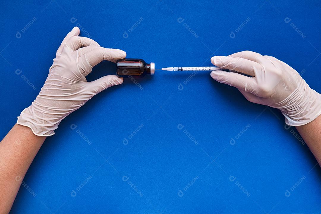 Imagem de uma enfermeira preparando a dose da vacina em fundo azul