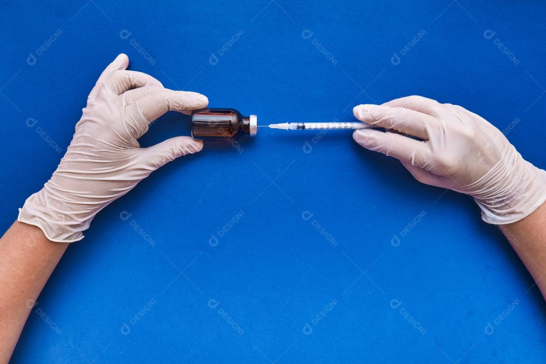 Imagem de uma enfermeira preparando a dose da vacina em fundo azul