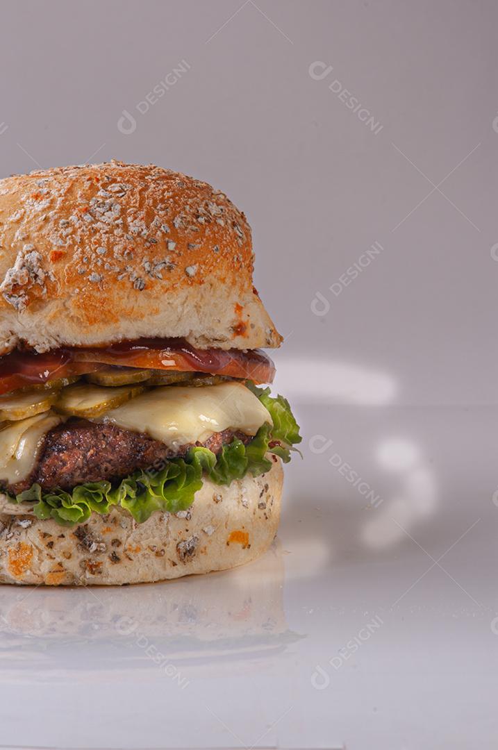 Hambúrguer com queijo derretido, maionese, alface, tomate, cebola em conserva no pão.