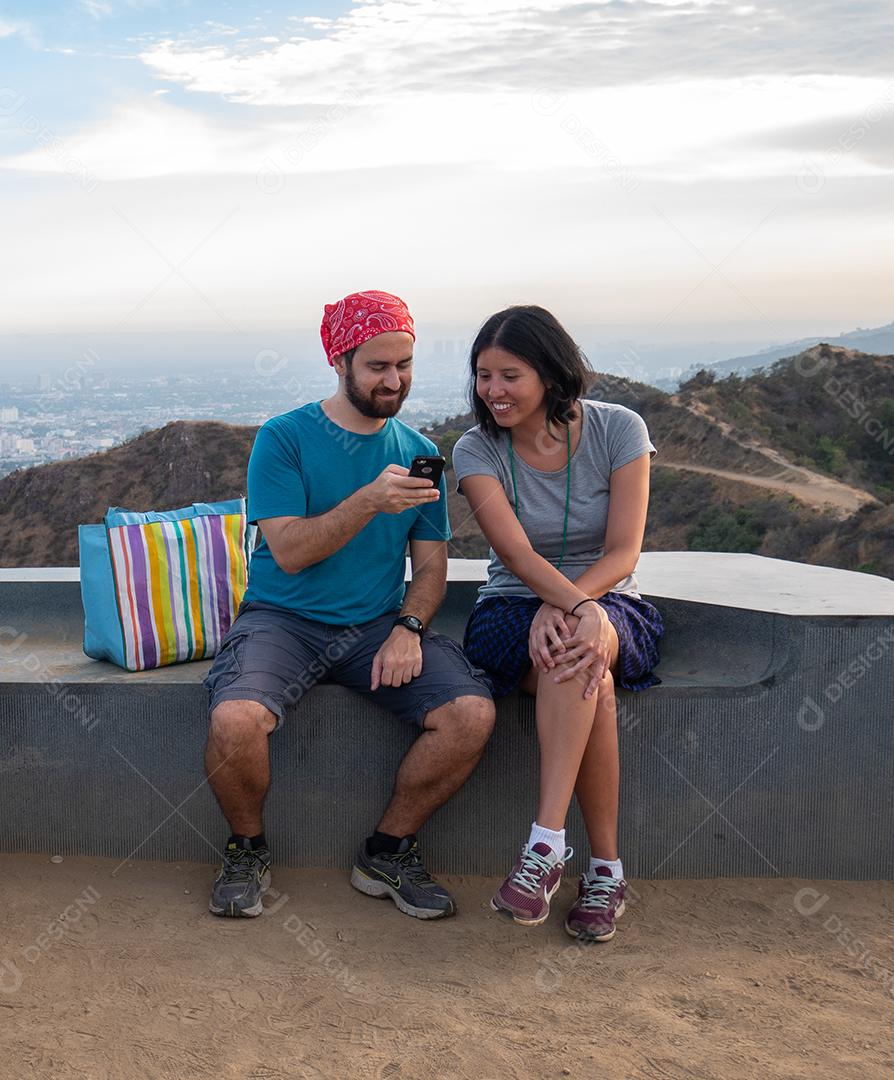 Vista de caminhadas casal no topo da viagem usando smartphone.