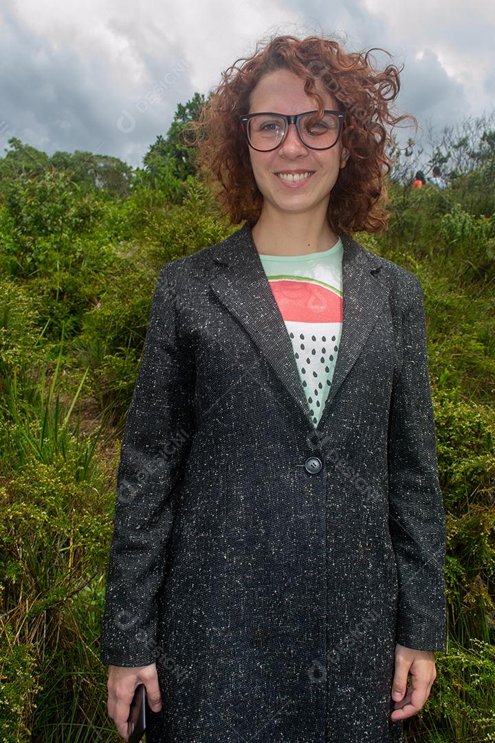 Linda mulher brasileira sorrindo e segurando o celular com floresta tropical ao fundo.