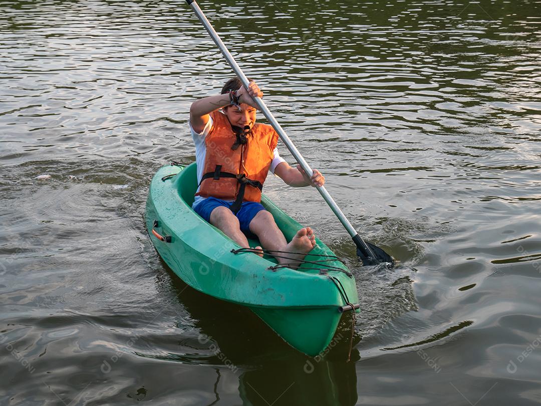 Menino se divertindo andando de caiaque no lago ao pôr do sol.