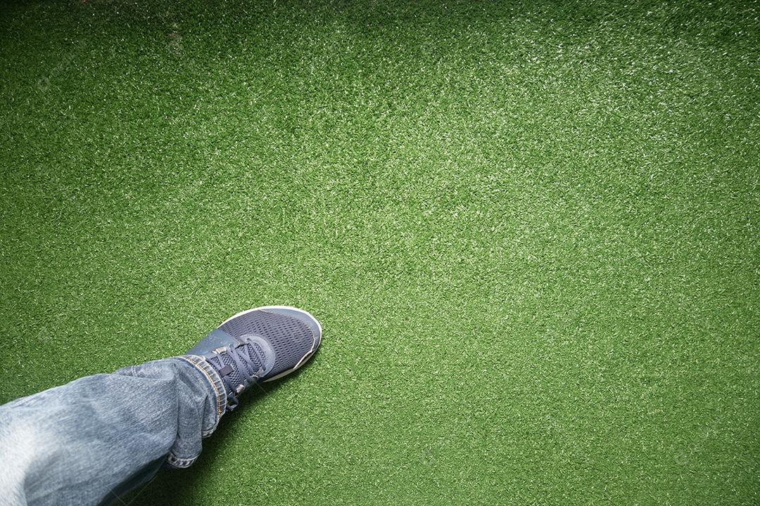 Vista superior da textura de grama verde artificial com pé entrando por baixo.