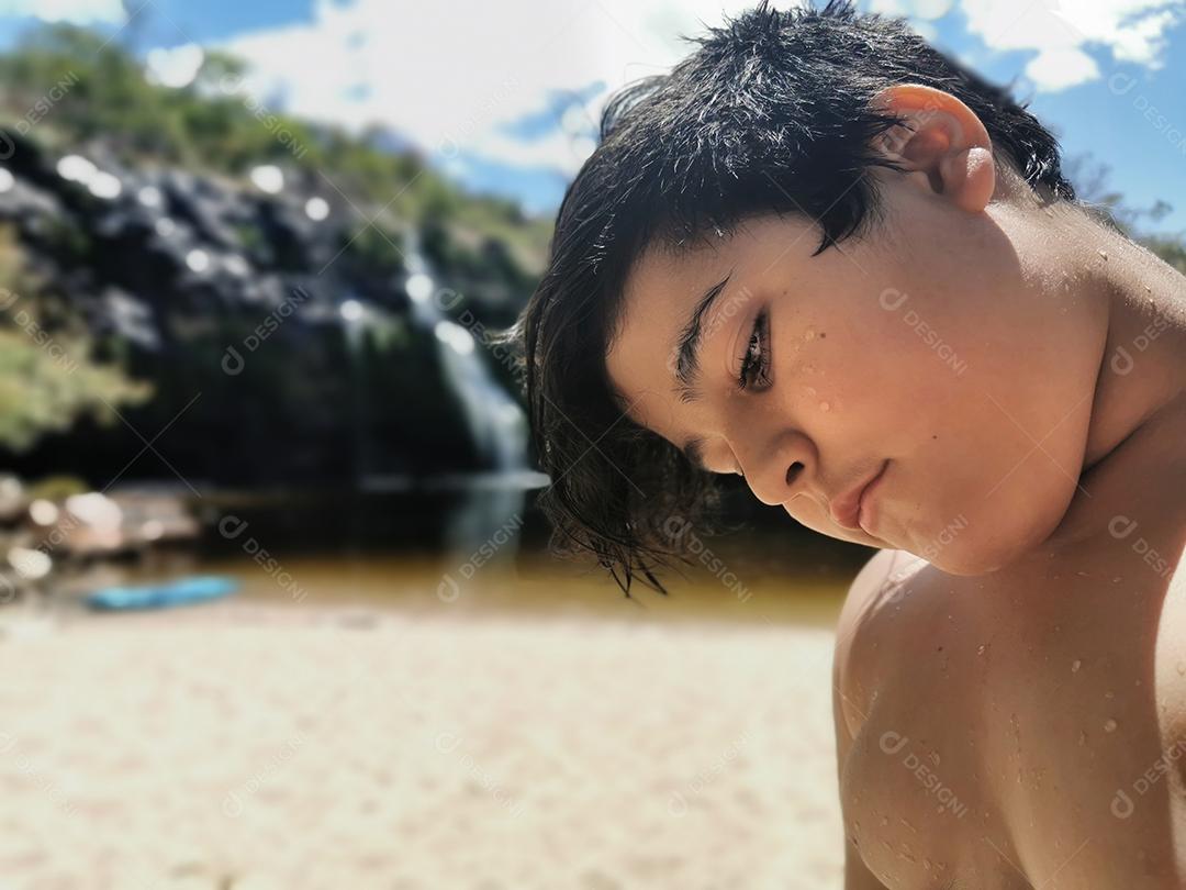 Garotinho no verão com cachoeira ao fundo.