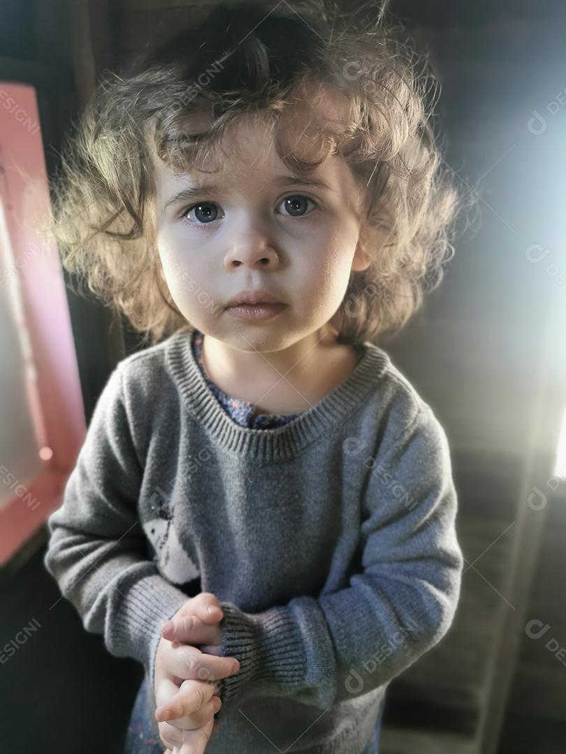 Menina bonita pequena olhando para a câmera com as mãos junto com reflexo de lente.