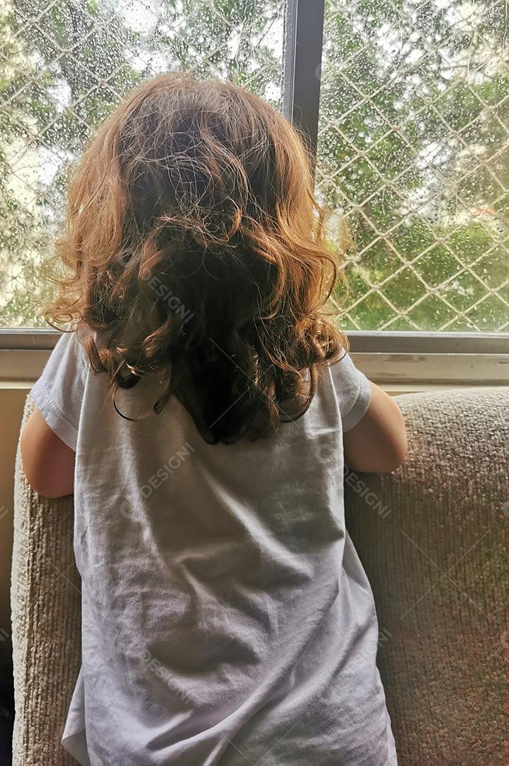 A menina olha a chuva pela janela..