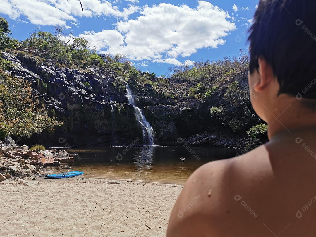 Garotinho no verão com cachoeira ao fundo com foco seletivo.