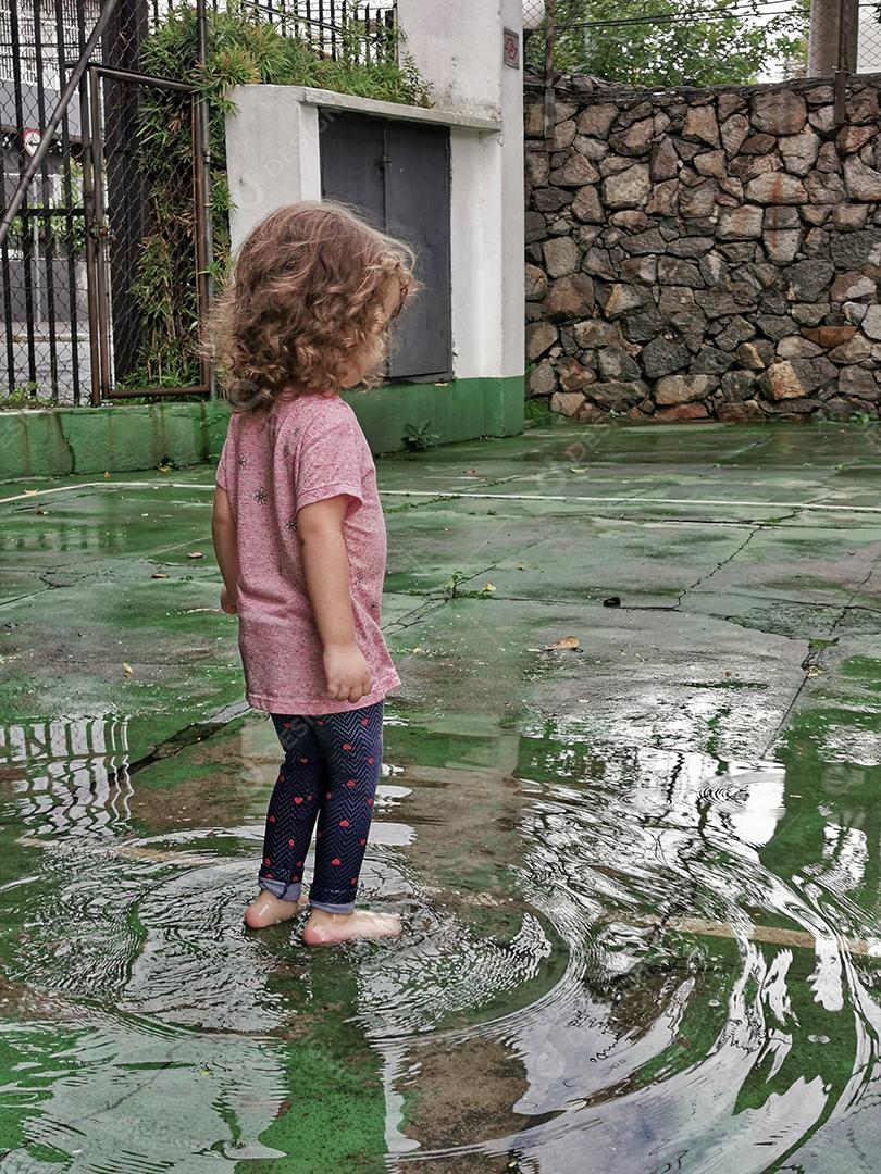 Vista da linda garota descalça jogando na poça depois da chuva.