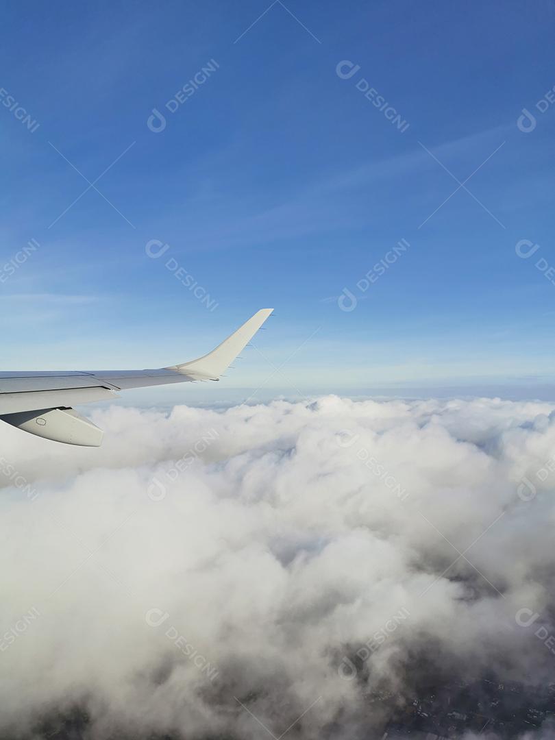 Visão vertical de nuvens brancas e fofas no céu azul sob a asa do avião.