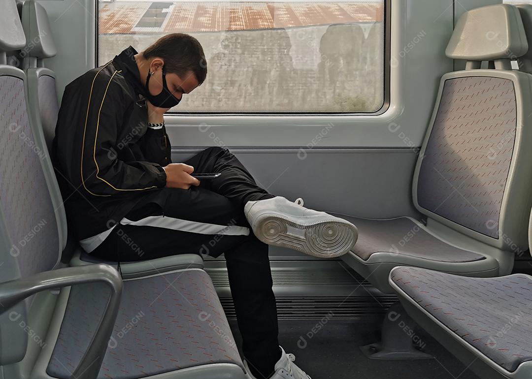 Vista do jovem sentado sozinho no assento do trem usando máscara.