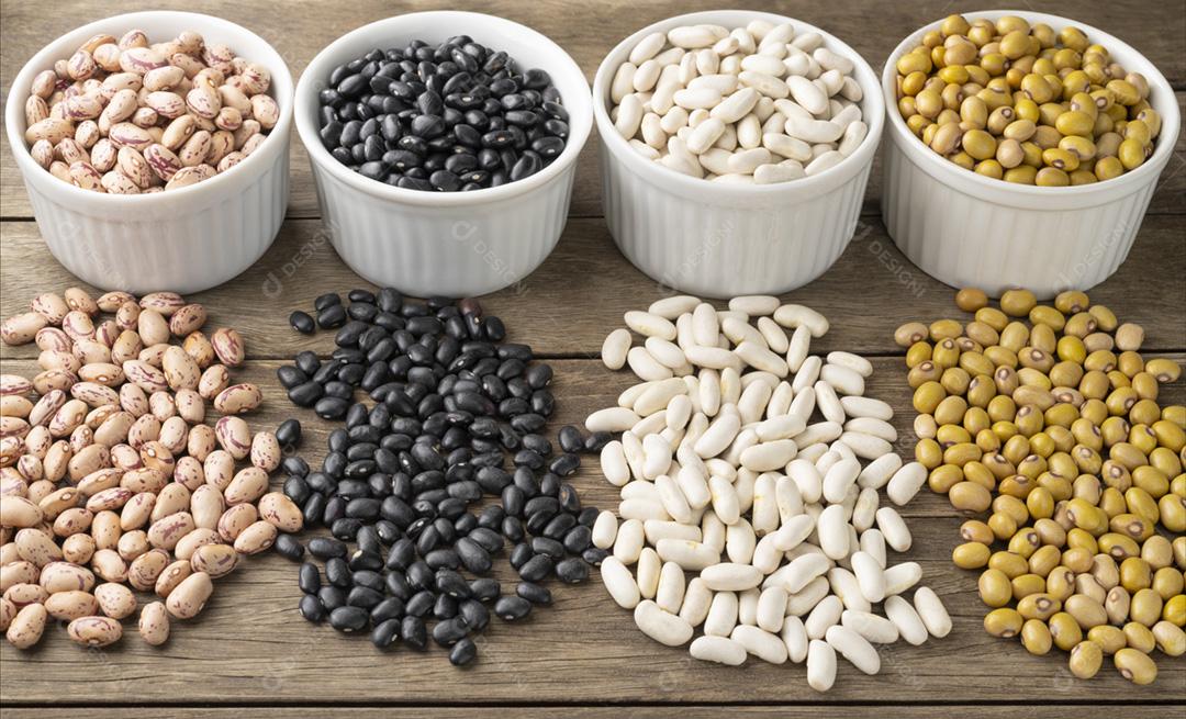 Closeup de feijões variados em tigelas brancas sobre a mesa de madeira
