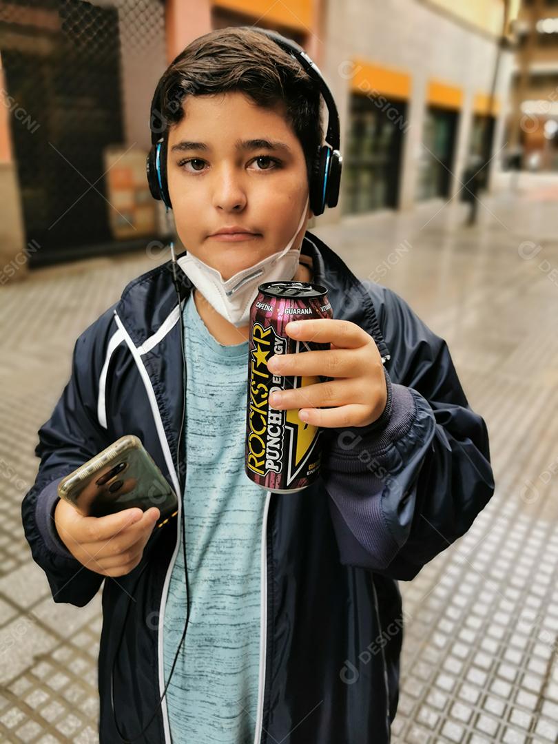 Málaga, Espanha - 22 de fevereiro de 2021: Vista de menino bebendo Rockstar e usando celular com máscara abaixada durante pandemia