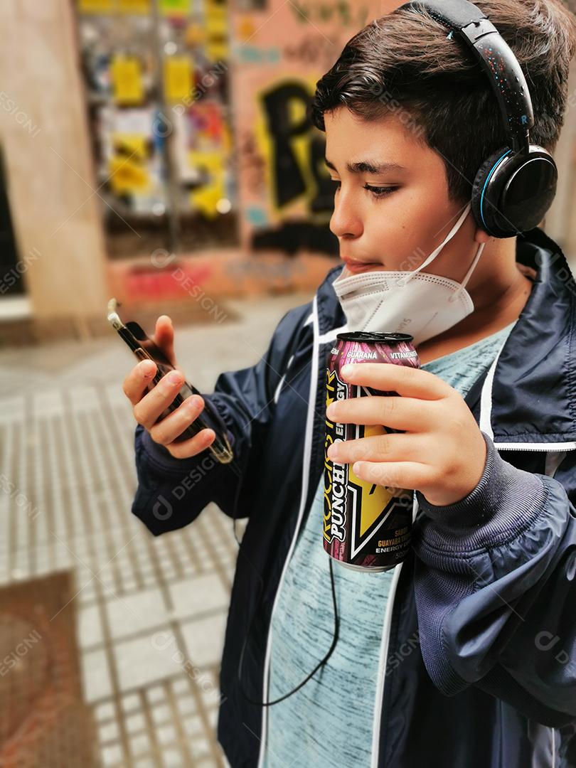 Málaga, Espanha - 22 de fevereiro de 2021: Vista de menino bebendo Rockstar e usando celular com máscara abaixada durante pandemia