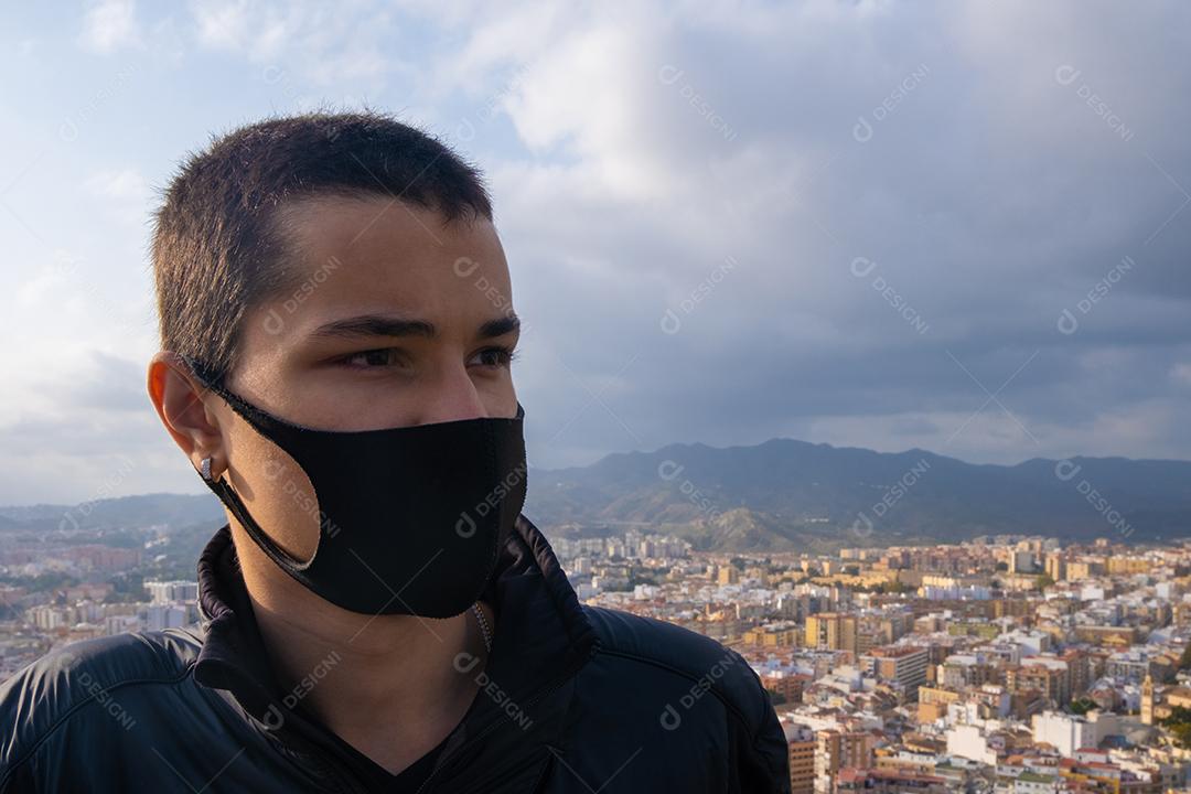 Rapaz usando máscara facial olhando para a cidade de Málaga de cima na Espanha.