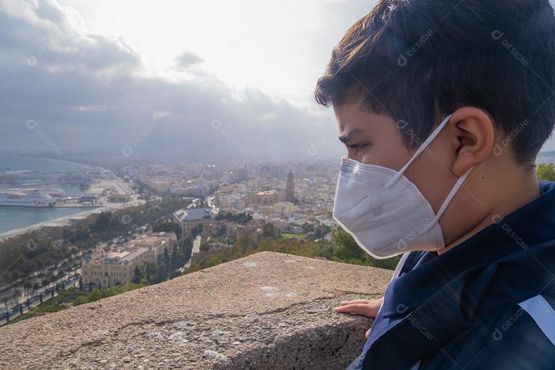 Menino usando máscara facial olhando de soslaio para a cidade de Málaga