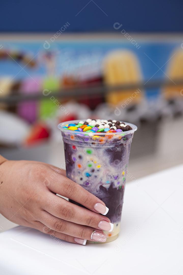 Mão de uma mulher segurando um copo plástico de açaí congelado. Copie o espaço.