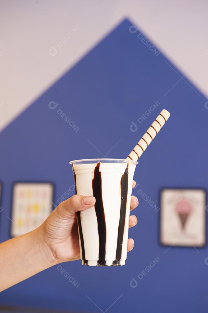 Mão de uma mulher segurando um copo plástico de milkshake de baunilha e chocolate