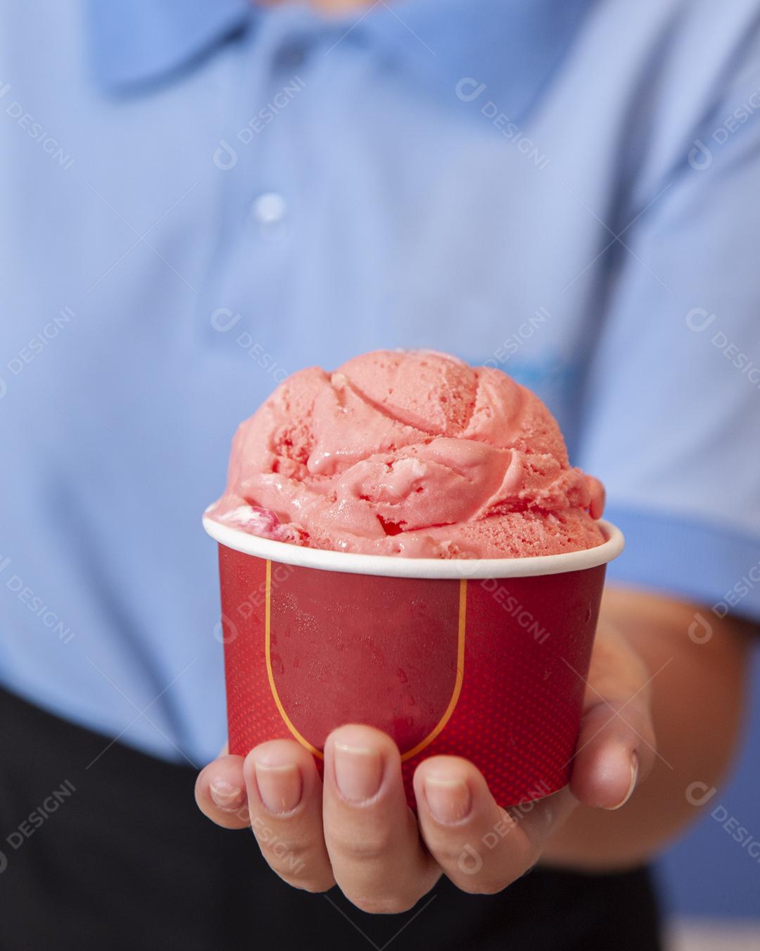 Mão de uma mulher segurando o copo com sorvete de morango.